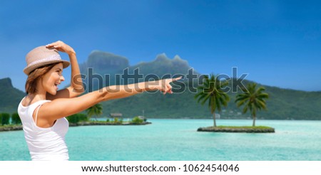 summer holidays, travel, people and vacation concept - happy young woman in hat pointing finger at touristic resort over exotic bora bora island beach background