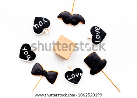 Gift for man on birthday. Gift box among cookies in shape of moustache, hat, bow tie and hearts with lettering love you on white background top view copy space