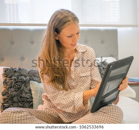 Young woman in pajamas using digital tablet in bed