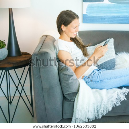 Happy young woman lying on sofa and text messaging on mobile phone