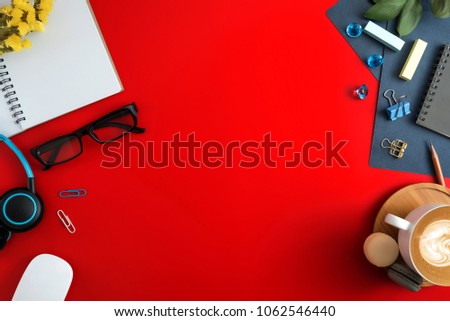 Flat lay, top view office table desk. Workspace with blank note book, keyboard, macaroon, office supplies, yellow flowers, green leaf, blue ornament and coffee cup on red background.