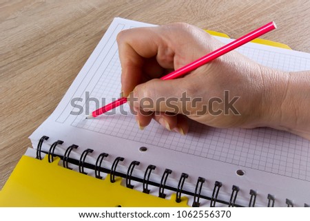 A hand with a pencil writes in a notebook