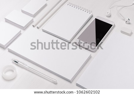 White blank stationery as work place with phone, earphone on light white wood background. 