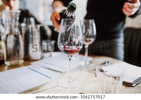 A close up shot of a sommelier pouring red wine into a wine glass. Selective focus point on the wine drops and the glasses. Other glasses in the background are out of focus. Wine training and tasting