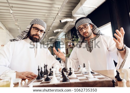 One arab businessman in thawb checkmates another playing chess at table at hotel room.