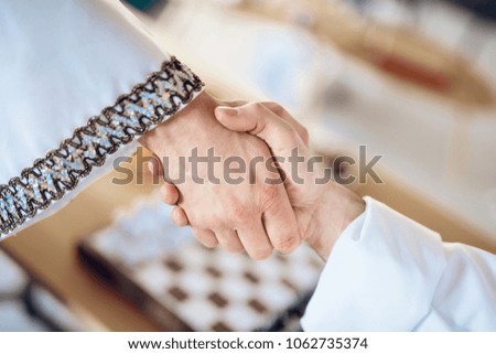 Close up two arab men shake hands with chessboard in background.