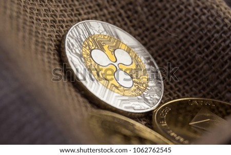 Close-up of Ripple golden/silver coin lying on rustic background together with other cryptocurrencies. Stylized as a treasure chest.
