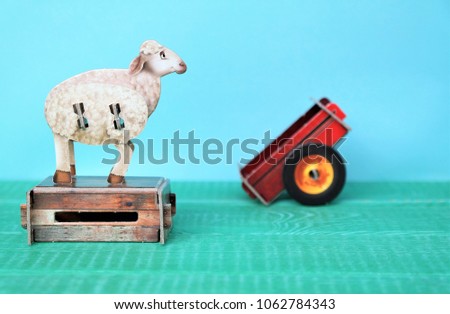 sheep is standing and waiting on a chest.
farm animal and red trailer.
small carton toys for children. 
blue background and copy space.
