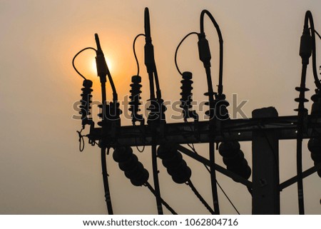 City electricity post pole during sunset with grey sky and sun in the background, silhouette