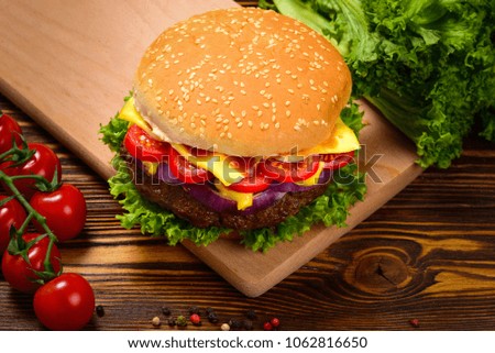 Delicious tasty burger with beef, tomatoes, salad and sauce on wooden table and black background.  Space for text or design.