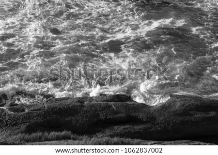 waves crashing on rocks causing foam effect in rio de janeiro macumba beach in photograph black and white