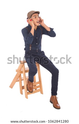 Handsome young man wearing a classic outfit, sitting on wood stairs, putting his earphone listening to music, isolated on white background