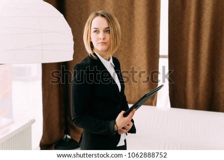 Confident young girl standing in the office holding a folder in her hands and looking away
