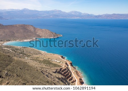 Crete landscape from above, blue sea and sky on a sunny day in background, rocks and green hills.