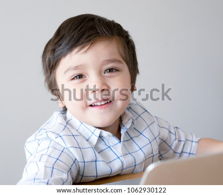 Cute little boy sitting on table playing game on computer, Smart kid looking at camera with smiling face, Children and Technology concept
