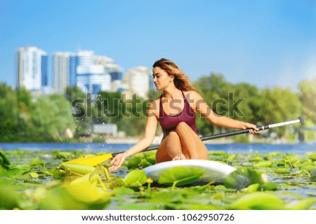 Beautiful sportive woman taking rest on the paddle board against city background