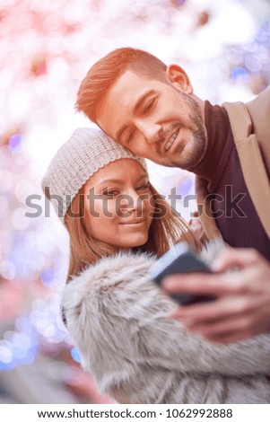 A beautiful young couple taking a selfie on the street with christmas lights in the background.