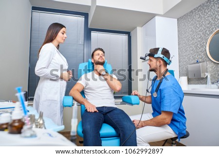 A handsome young patient in pain consulting with the doctor and his assistant in the hospital room.