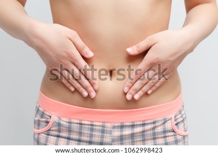 Concept of early term of pregnancy. Close up photo of woman's abdomen and belly button, she is touching her slim stomach with two hands. isolated on white background Royalty-Free Stock Photo #1062998423