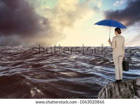 Rear view of businesswoman standing on rock holding blue umbrella and briefcase looking at sea again