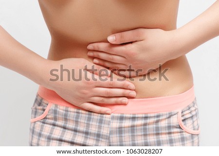 Young woman with hands on her belly on a gray background, closeup