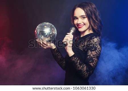 lifestyle and people concept: Young woman wearing black dress, holding disco ball  and  singing into microphone  