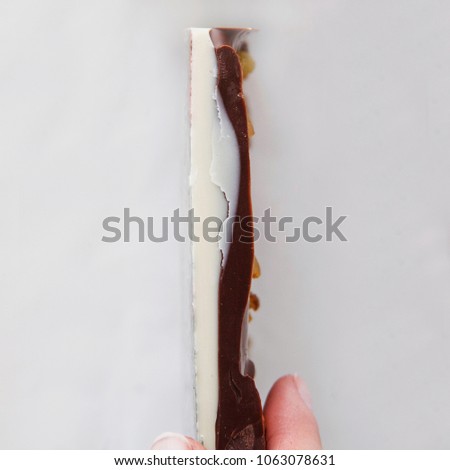 Side of twisted white and dark milk chocolate bar. Cut of chocolate. White background. Horizontal view. Free space for text. Womans hand holds chocolate.