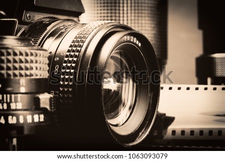 Black and white image of vintage professional cameras,lenses and a film roll