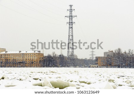 A power line tower on the bank of a frozen river during a snowfall