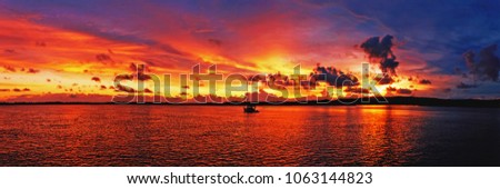 A spectacular inspirational brightly coloured cloudy sea water tropical panoramic sunrise seascape featuring silhouettes with ocean water reflections. Queensland, Australia.