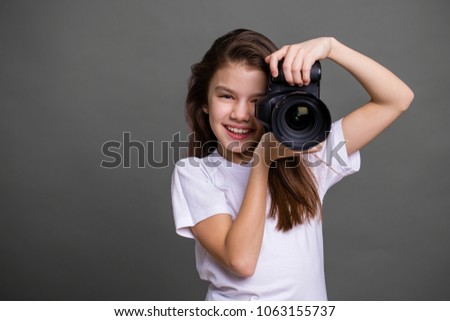 Cute brunette little girl holding an photo camera, isolated on gray background
