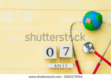 Wooden Block calendar for World health day, April 7. Healthcare and medical concept. Red heart with Stethoscope, handmade globe on Pastel white and blue wooden table background texture.
