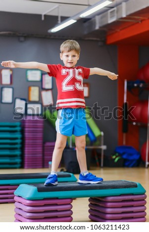 a boy in a red t-shirt stands, spreading his hands to the sides in the gym