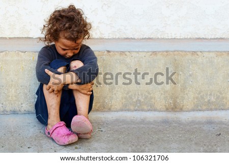 poor, sad little child girl sitting against the concrete wall Royalty-Free Stock Photo #106321706