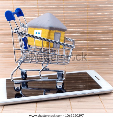 Small shopping basket cart with the house on tablet computer on background of wooden fence. Idea: Image for property real estate investment concept. Home for sale in market.