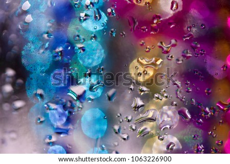 Colorful defocused abstract composed of macro captured water droplets on glass with illuminated multi-color bokeh in background
