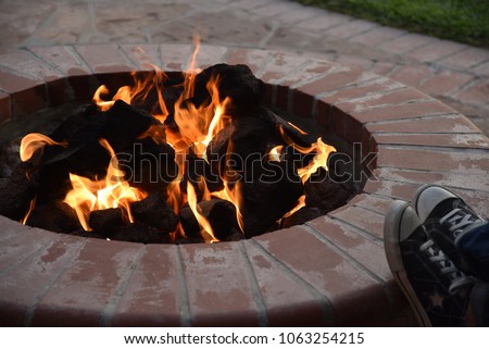 A picture of a brick backyard fire pit with someone resting their feet on the edge