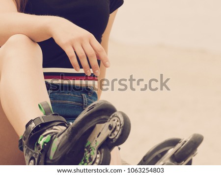 Woman slim legs wearing roller skates sitting outside. Sport activity, workout and exercising concept.