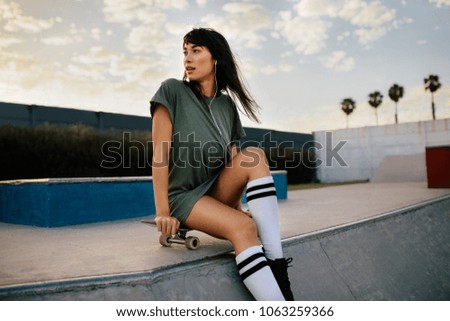 Female skateboarder at skate park. Woman sitting on the her skateboard and looking away.