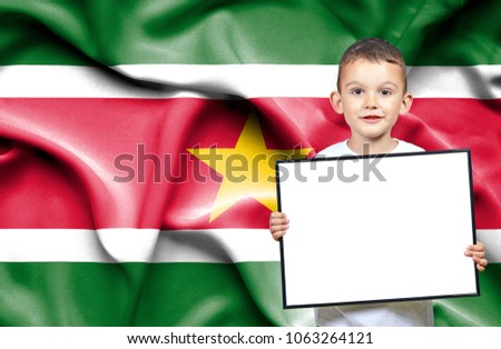 Cute small boy holding emtpy sign in front of flag of Suriname