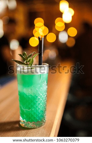 Close-up green cocktail with lime and mint on the bar, blurred background.