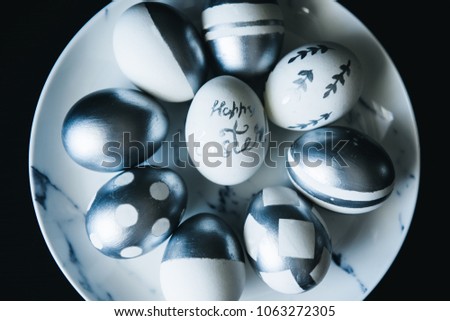 Group of diverse silver Easter eggs in a marble plate  on black background, original stylish idea, selective focus