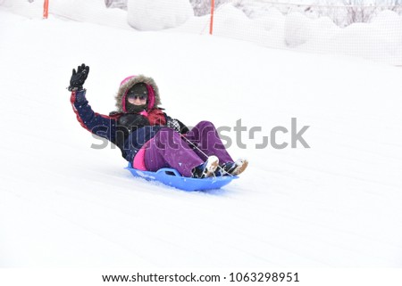 A girl is playing sled on snow, and wave her hand to camera, show feeling of fun