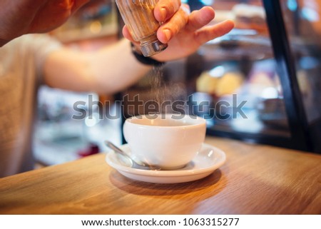 barista pours cinnamon into coffee in coffeeshop