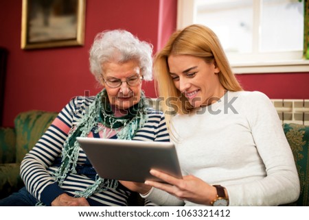 Two generation using tablet and smiling together, granddaughter learn grandmother how to use electronics