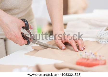 Workplace of seamstress. Dressmaker cuts dress detail with scissors Royalty-Free Stock Photo #1063321535