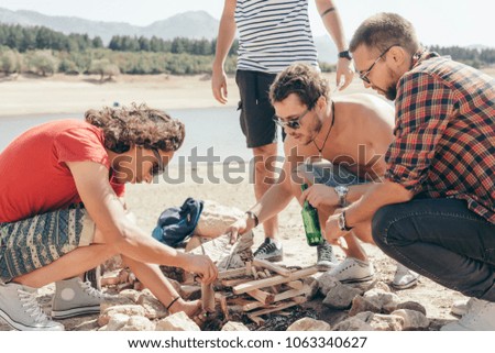 Picnic holiday concept. Group of friends preparing a bonfire and relaxing by a lake.
