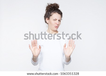 Body language. Disgusted stressed out beautiful young woman with hair knot posing at studio wall, keeping hands in stop gesture, grimacing, trying to defend herself as if saying: Stay away from me. Royalty-Free Stock Photo #1063351328