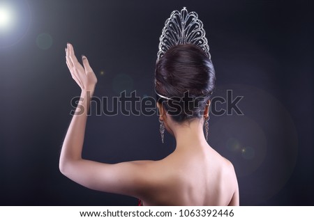 Back rear side view Portrait of Miss Pageant Beauty Contest in Red sequin Evening Gown with Diamond Crown wave hand, Asian Woman fashion make up hair style, studio lighting dark background copy space Royalty-Free Stock Photo #1063392446