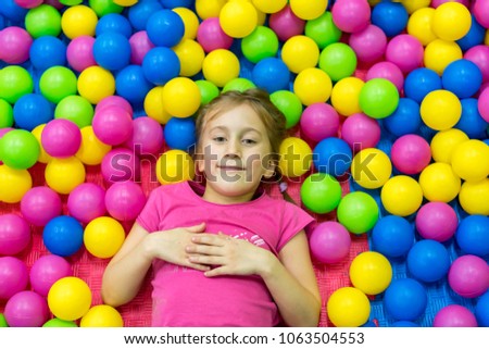Cute and pretty little girl looking at camera inside heap of multi-colored balloons